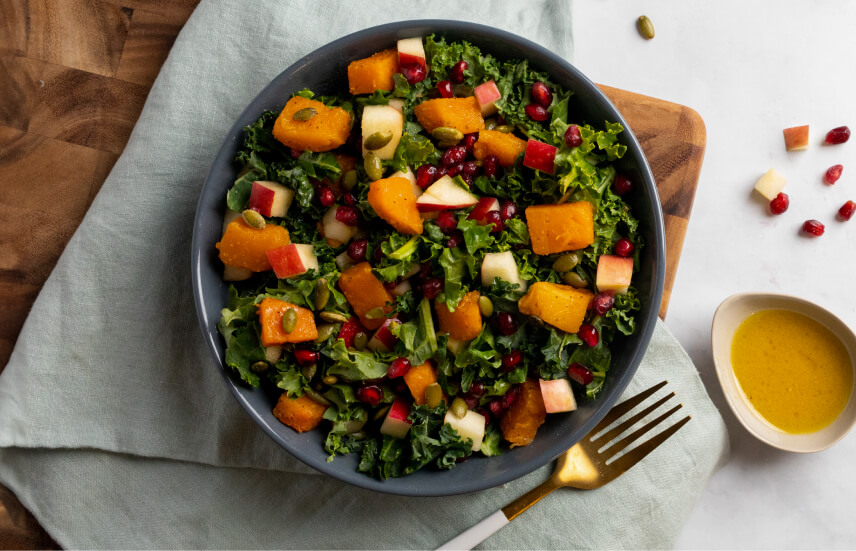 A salad in a blue bowl on a cutting board with white linens