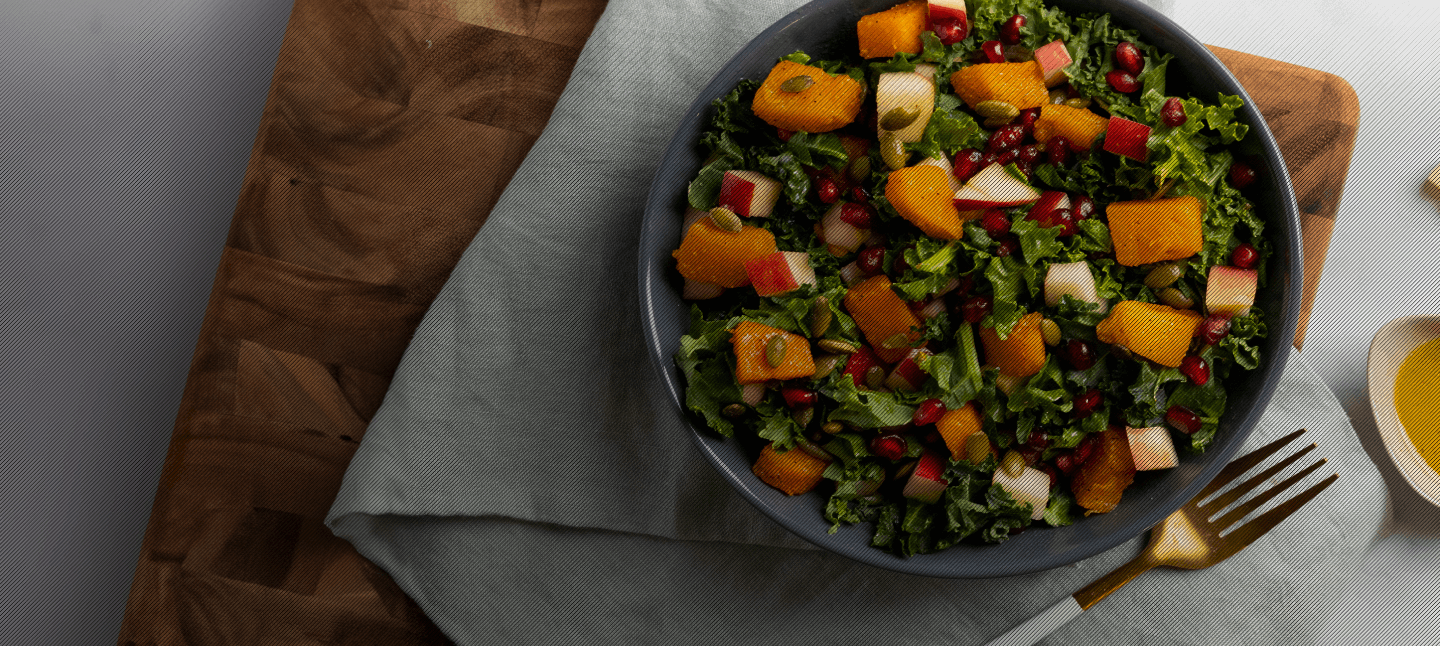 A salad in a blue bowl on a cutting board with white linens